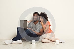 Shocked couple using laptop, sitting on floor