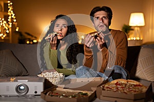 Shocked Couple Watching Horror Movie And Eating Pizza Sitting Indoors