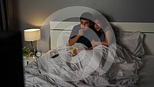 Shocked couple is watching horror movie TV on a bed at night