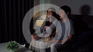 Shocked couple is watching horror movie tv on sofa at night
