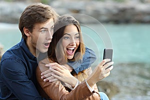 Shocked couple watching a smart phone on holidays