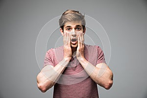 Shocked dazed young man holding head with both hands over grey background