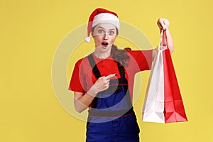 Shocked delivery woman holding pointing at shopping bags, offering free shipping from fashion store.