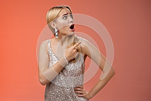 Shocked displeased bothered arrogant blond glamour woman in silver glittering dress turning upper right corner pointing