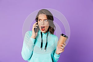 Shocked displeased young woman posing isolated over purple background wall talking by mobile phone