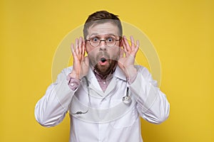 Shocked doctor has hands to ears and listens to secret conversations or gossip with an open mouth and big eyes.