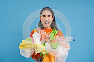 Shocked eco activist, collects loads of plastic to recycle, looking upset at bottles and unsorted garbage, blue