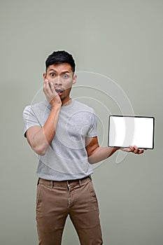 Shocked and excited Asian man covering his cheek and holding a tablet mockup