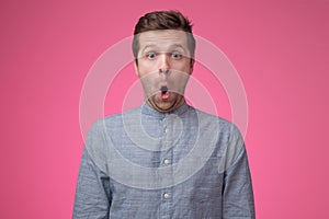 Shocked face of caucasian man in blue shirt on pink background