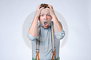 Shocked face of young european man in blue shirt and suspenders