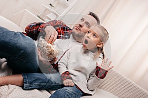 shocked father and daughter eating popcorn and watching tv together photo
