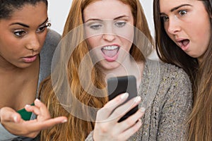 Shocked female friends looking at mobile phone together