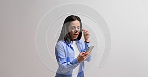 Shocked female professional looking out through eyeglasses and reading unexpected message on mobile phone. Amazed businesswoman photo