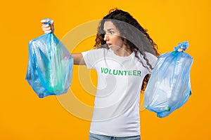 Shocked Female Volunteer Holding Unsorted Plastic Garbage, Over Yellow Background