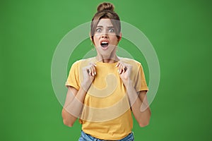 Shocked feminine glamour woman with combed hair in yellow t-shirt frowning gasping with opened mouth holding palms