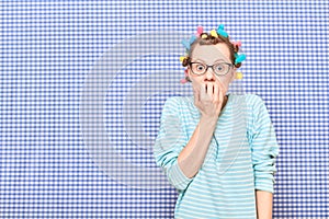 Shocked frightened woman with bright hair curlers is biting nails