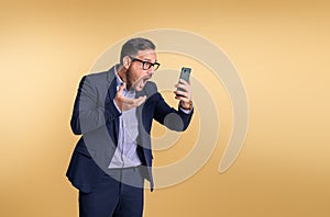 Shocked frustrated young male professional manager dressed in elegant suit looking at mobile phone and gesturing. Business manager