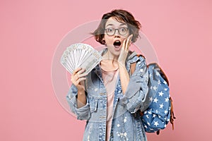 Shocked girl student in denim clothes glasses backpack isolated on pastel pink background. Education in school