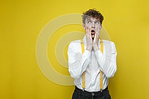 shocked guy in festive outfit is surprised and looks away at the copy space on yellow background, amazing nerd student