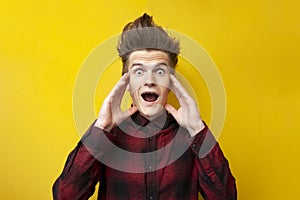 Shocked guy screaming on a yellow isolated background, hipster with a funny hairstyle is panicking, close-up