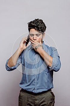Shocked handsome businessman in formals anxious on a phone call while talking to client in grey background