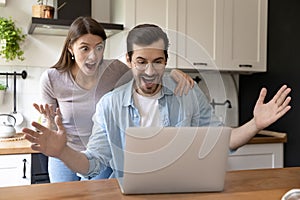Shocked happy young family couple looking at computer screen.