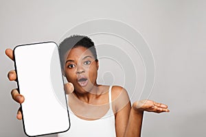 Shocked healthy woman holding smartphone with white empty blank screen display on gray studio wall background. Happy model