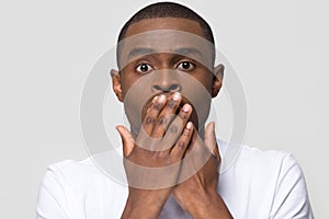 Shocked horrified african man covering mouth with hands feel scared photo