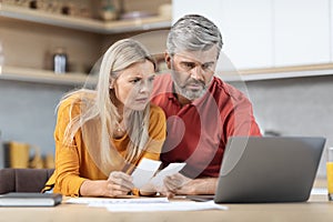 Shocked husband and wife sitting at kitchen table, counting spendings