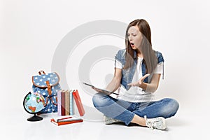 Shocked irritated woman student holding using tablet pc computer, spreading hand, sitting near globe, backpack, school