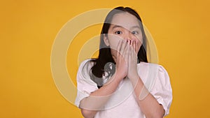 Shocked little asian girl feeling surprised, closing her mouth in amazement, orange background