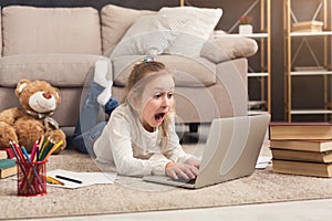 Shocked little girl watching movie on laptop