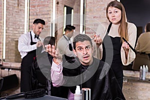Shocked man with apologetic hairdresser at barbershop photo