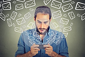 Shocked man busy sending messages emails from smart phone email icons flying of mobile phone