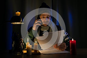 Shocked man in candle light looking at high bills for electricity, gas heating in cold dark room at home. energy crisis, household