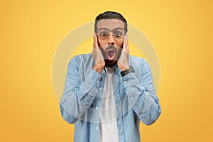 Shocked man with hands on cheeks on yellow