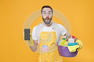 Shocked man househusband in rubber gloves hold basin detergent bottles washing cleansers doing housework isolated on