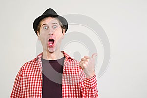 Shocked man keeps mouth widely opened, expresses surprisment and disbelief, shows something with thumb on blank copy space.