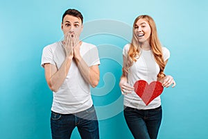 Shocked man, learns about the pregnancy of his wife, a pregnant woman holding a red paper heart against the belly