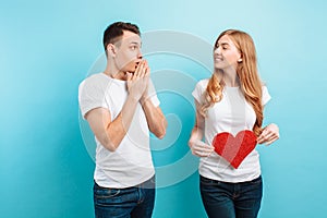 Shocked man, learns about the pregnancy of his wife, a pregnant woman holding a red paper heart against the belly