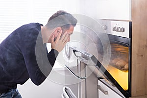 Shocked Man Looking At Burnt Cookies In Oven
