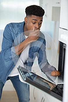 shocked man looking at burnt cookies in oven