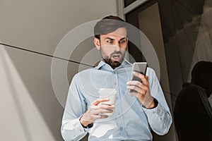 Šokovaný muž je pozerá na telefón obrazovka počas káva rozbiť 