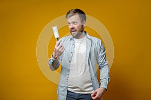 Shocked man looking at roll with duct tape, which had just cleaned his clothes from animal hair, on a yellow background.