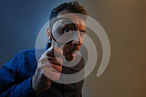 Shocked man with magnifying glass on grey background. Curious young man with magnifying glass Isolated on grey background