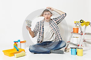Shocked man in newspaper hat holds bundle of dollars, cash money. Instruments for renovation apartment isolated on white