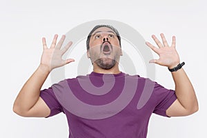 A shocked man put his hands upon seeing something up in the air. Wearing a purple waffle shirt. Isolated on a white background