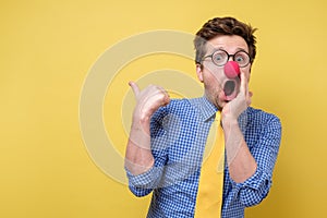 Shocked man with red clown nose looking camera showing pointing on copyspace. Clown, corcus or show concept.