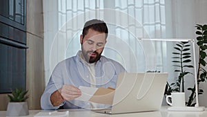 Shocked man staring at letter and leaning head on hand at home workplace