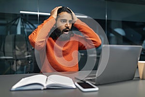 Shocked millennial eastern businessman in dark office